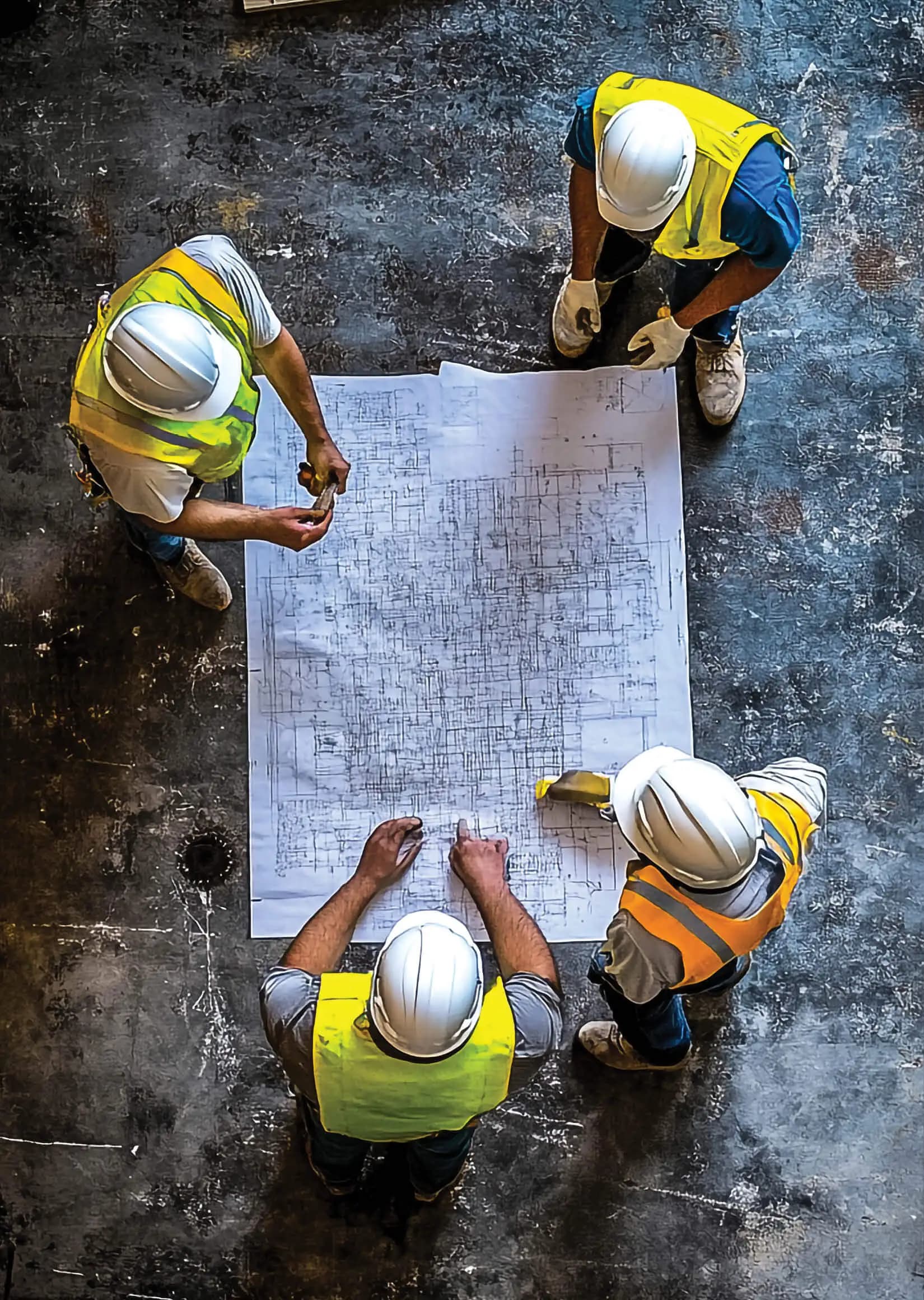 A crew in hard hats reviewing plans laid out on the ground